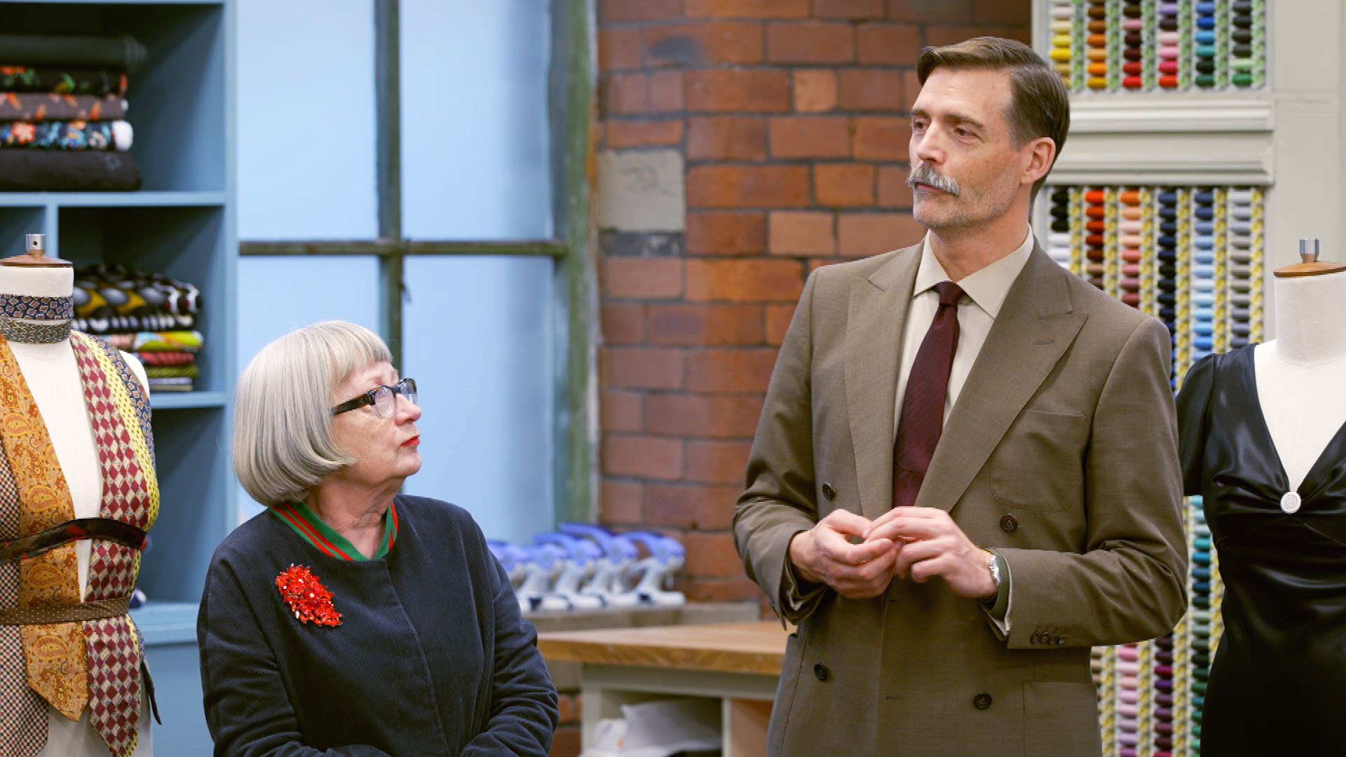  Esme Young and Patrick Grant standing in the sewing room chatting 
