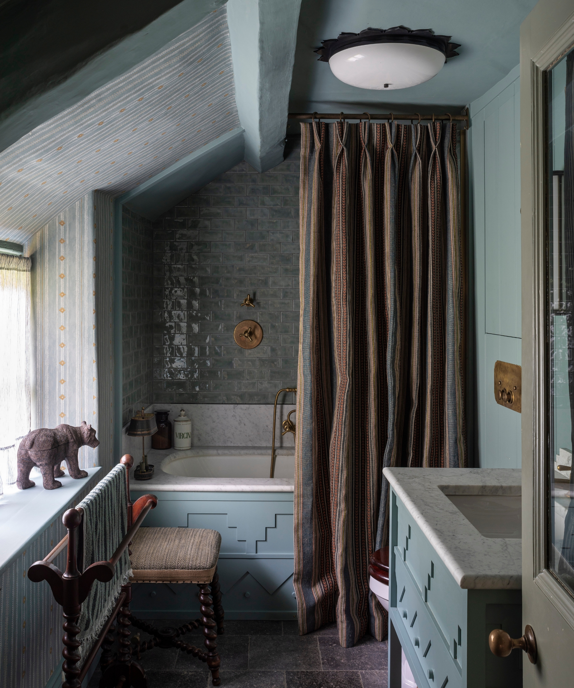 A blue bathroom with a striped shower curtain hung from the ceiling