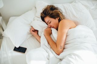 Woman asleep in bed, away from phone, as it's one of the reasons why people why can't lose weight