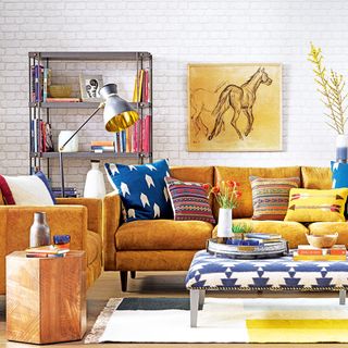 White living room with tan sofa and colourful patterned cushions with small tables on patterned rug