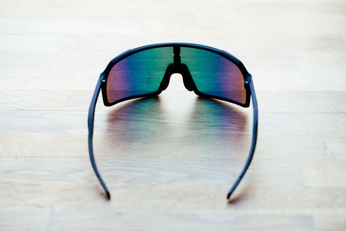 A set of black frame sunglasses with irridescent lenses on a wooden surface