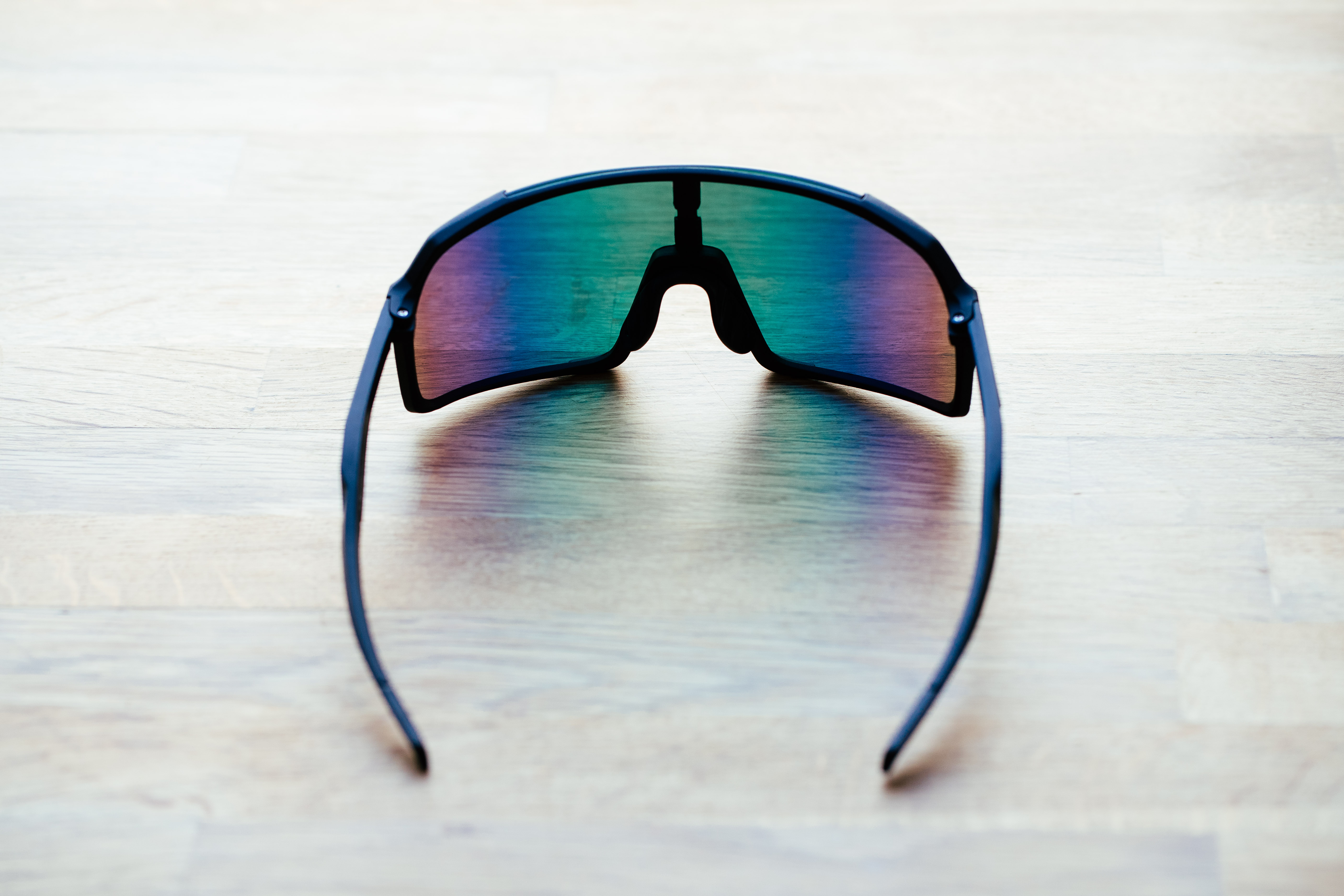 A set of black frame sunglasses with irridescent lenses on a wooden surface