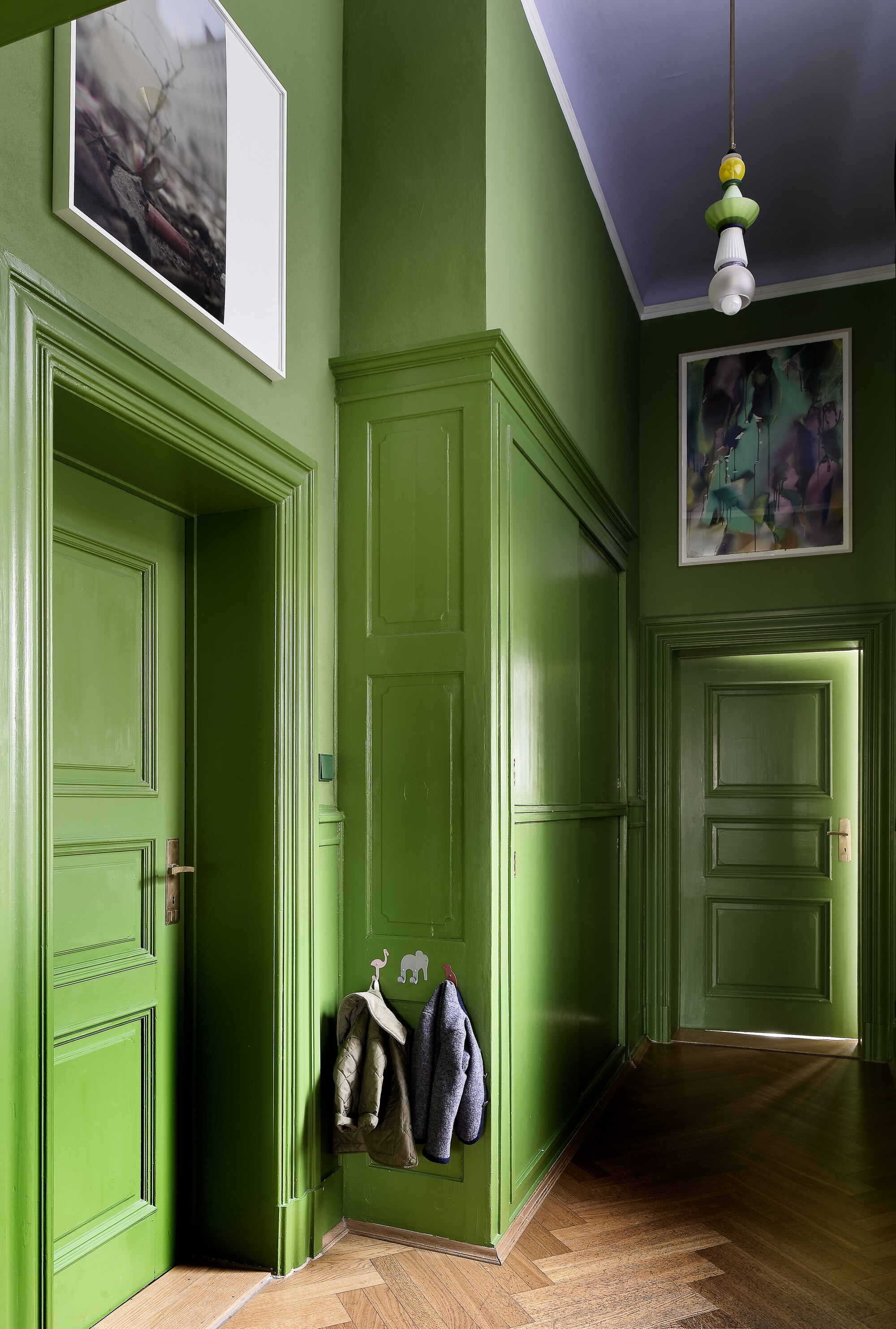 bright green paint on hallway walls with herringbone floors, panelling, and artwork, with purple ceiling, and pendant light