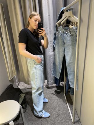Woman in dressing room wears black t-shirt, blue jeans, blue trainers