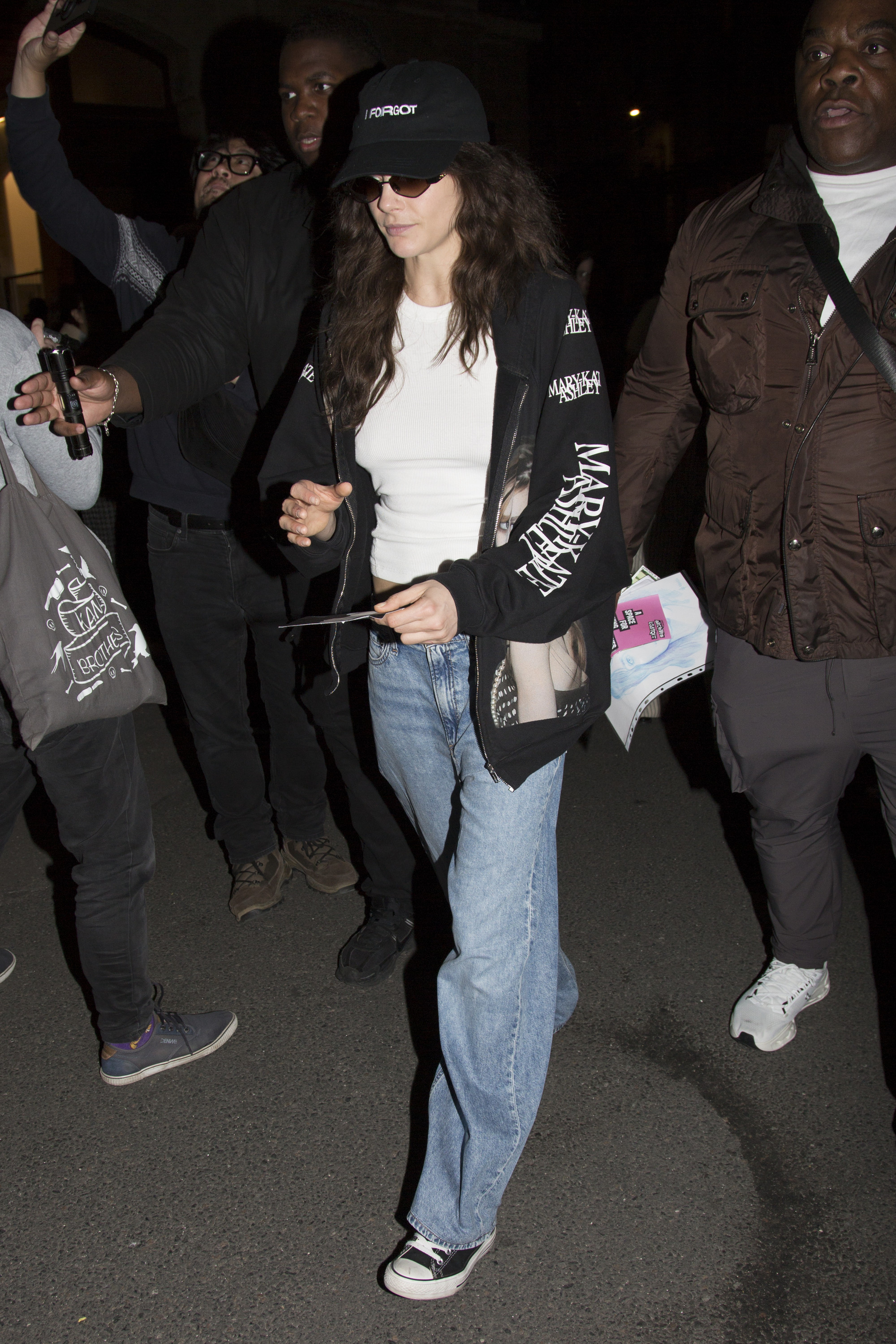 Cara Delevingne wears straight leg jeans with a black hoodie and black converse trainers.