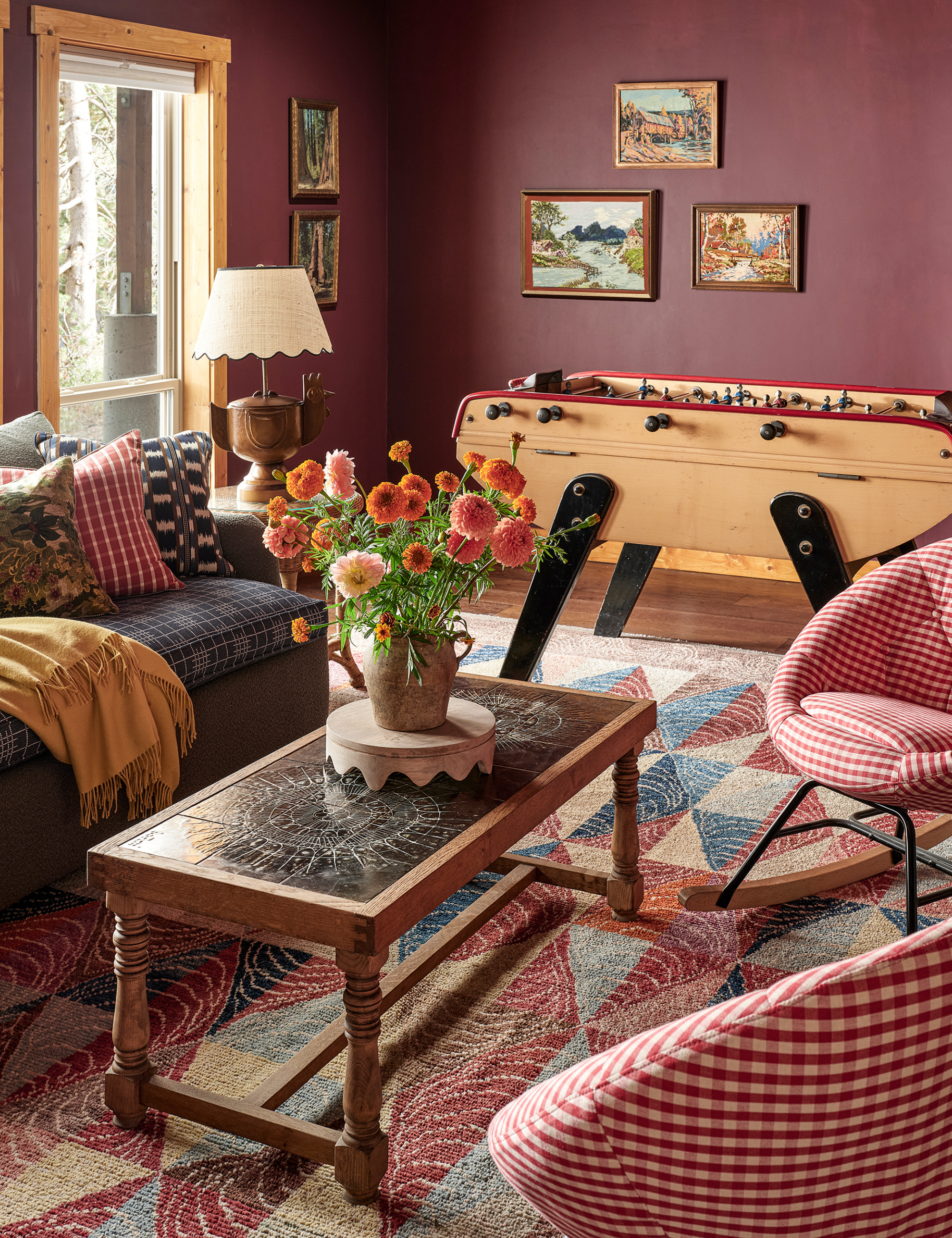 Pattern-filled family room offsetting an Italian foosball table with a layered mix, including a patchwork-style rug, geometric throw pillow trio, and red gingham chairs