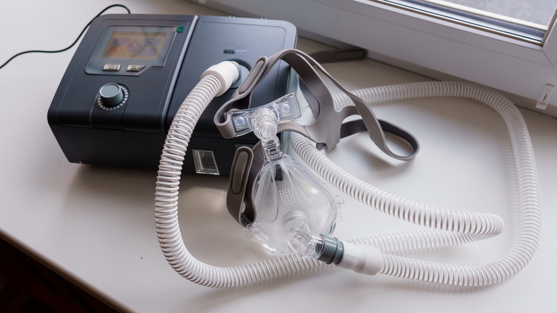 A breathing mask connected to a black box with a white, flexible tube.