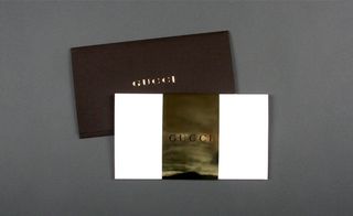 View of Gucci's brown, white and gold two-part invitation pictured against a grey background