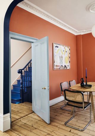 dining room with orange walls and wooden floor and wooden table and blue staircase