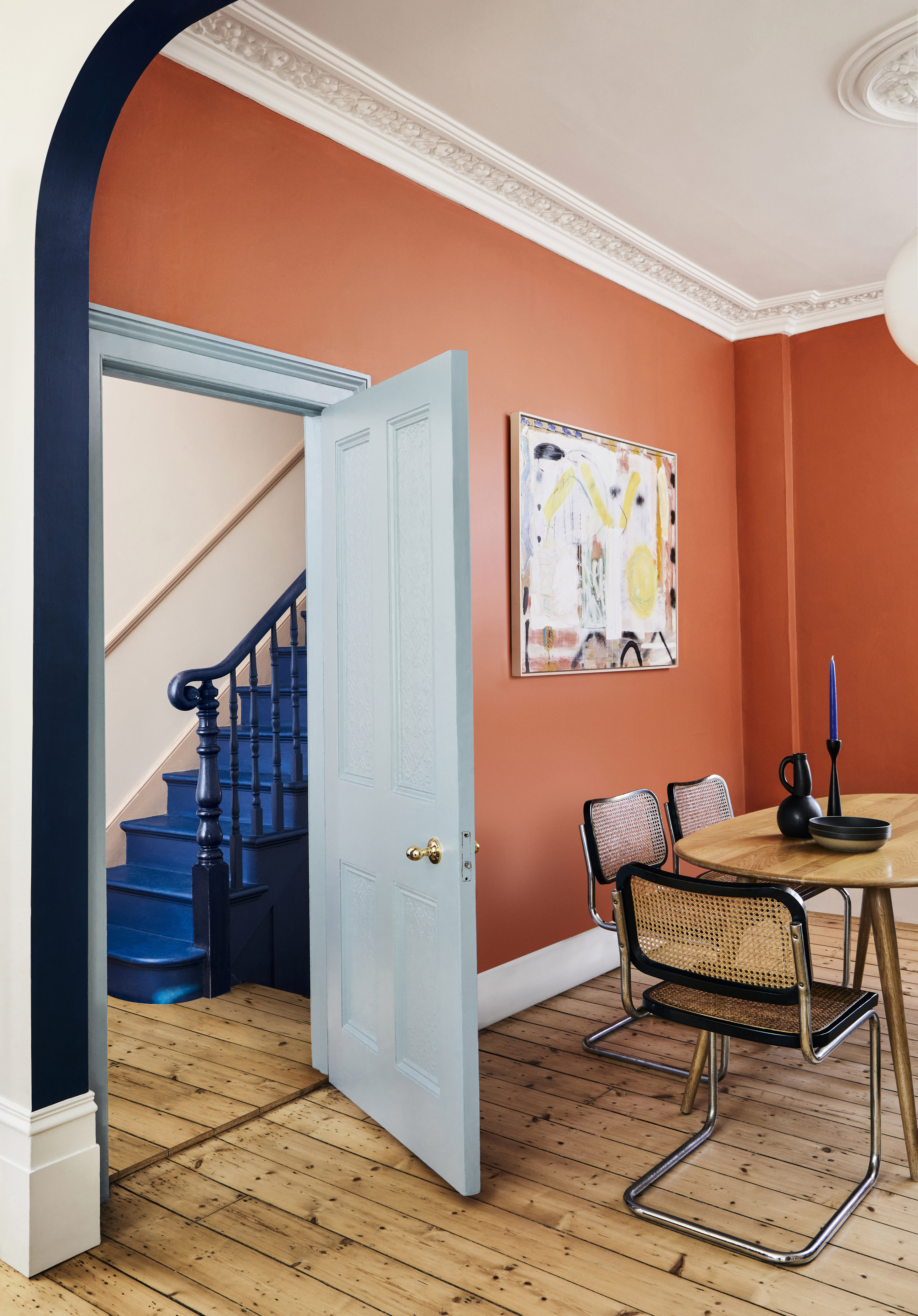 dining room with orange walls and wooden floor and wooden table and blue staircase