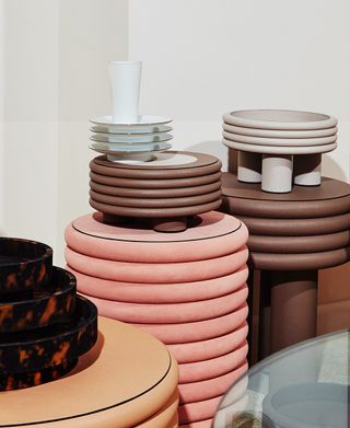 Four different styles of tableware (plates). Three different sized lava-style bowls. A pile of five brown border plates. A pile of four grey border plates. A pile of four white ceramic bowls.