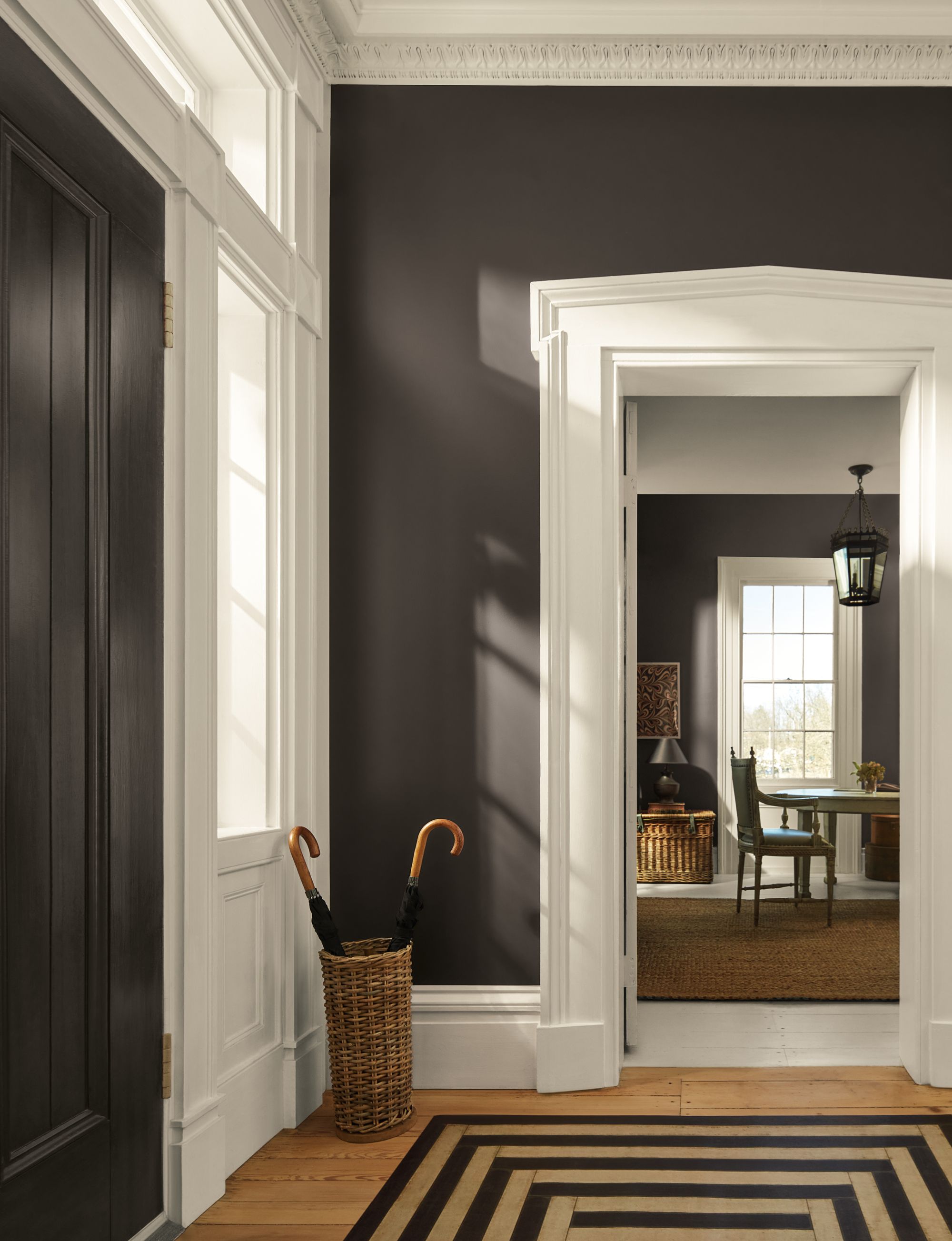 An entryway painted in a dark gray-brown paint color with thick white trim and a woven umbrella basket