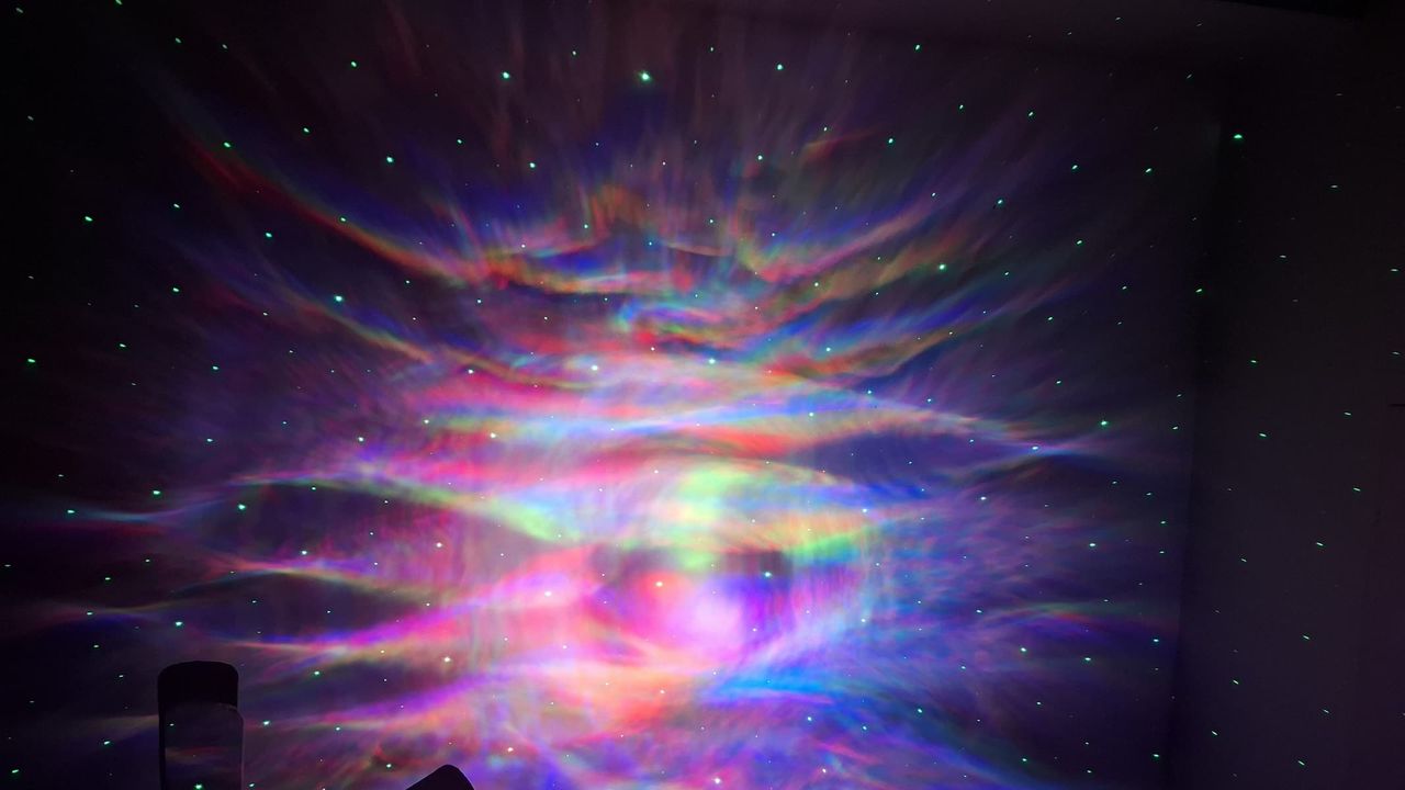 A multicolor projection with dots representing stars is on a wall in a dark room.