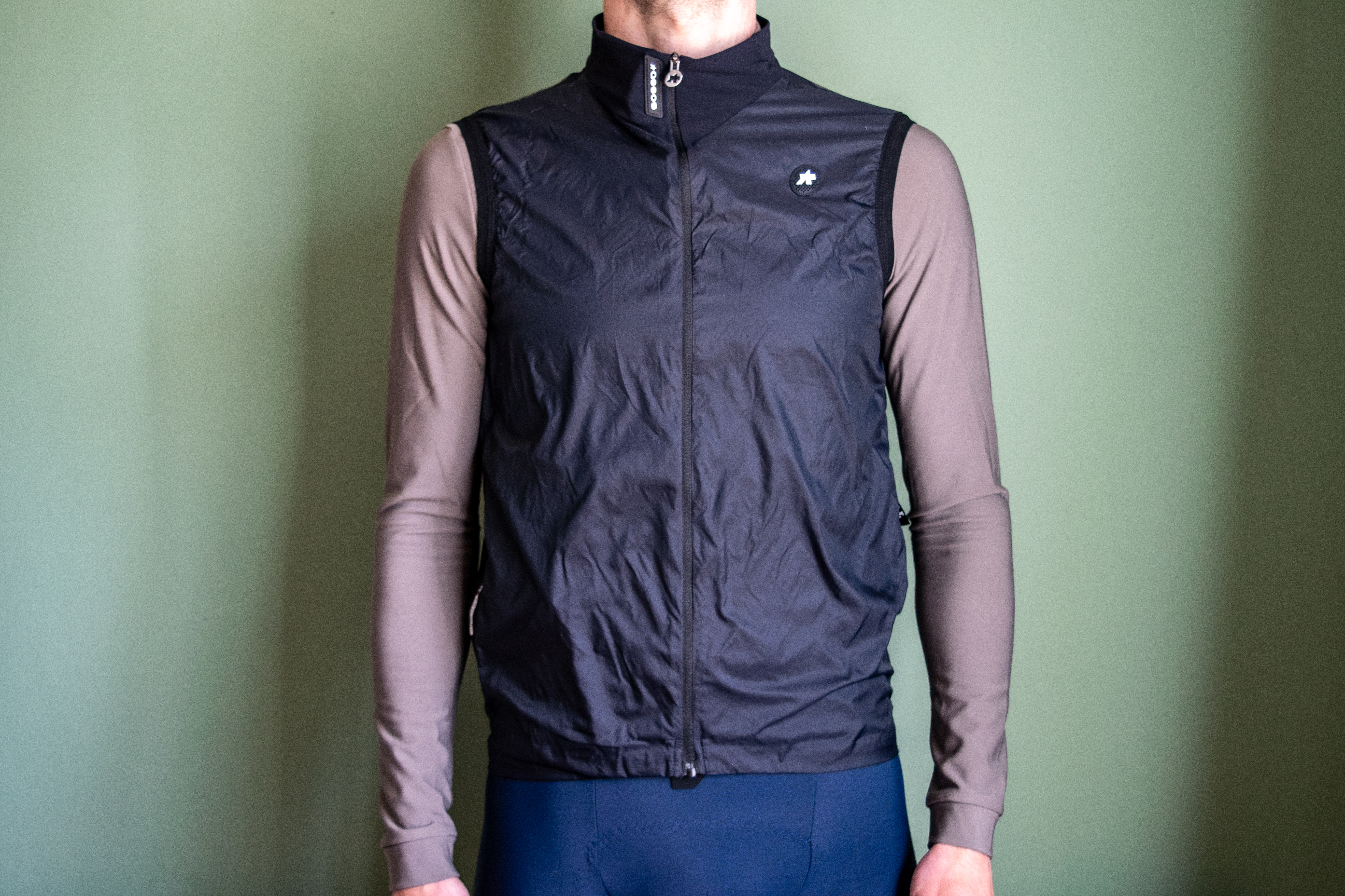 A man wearing a black Assos Tactica gilet over a grey long sleeve shirt