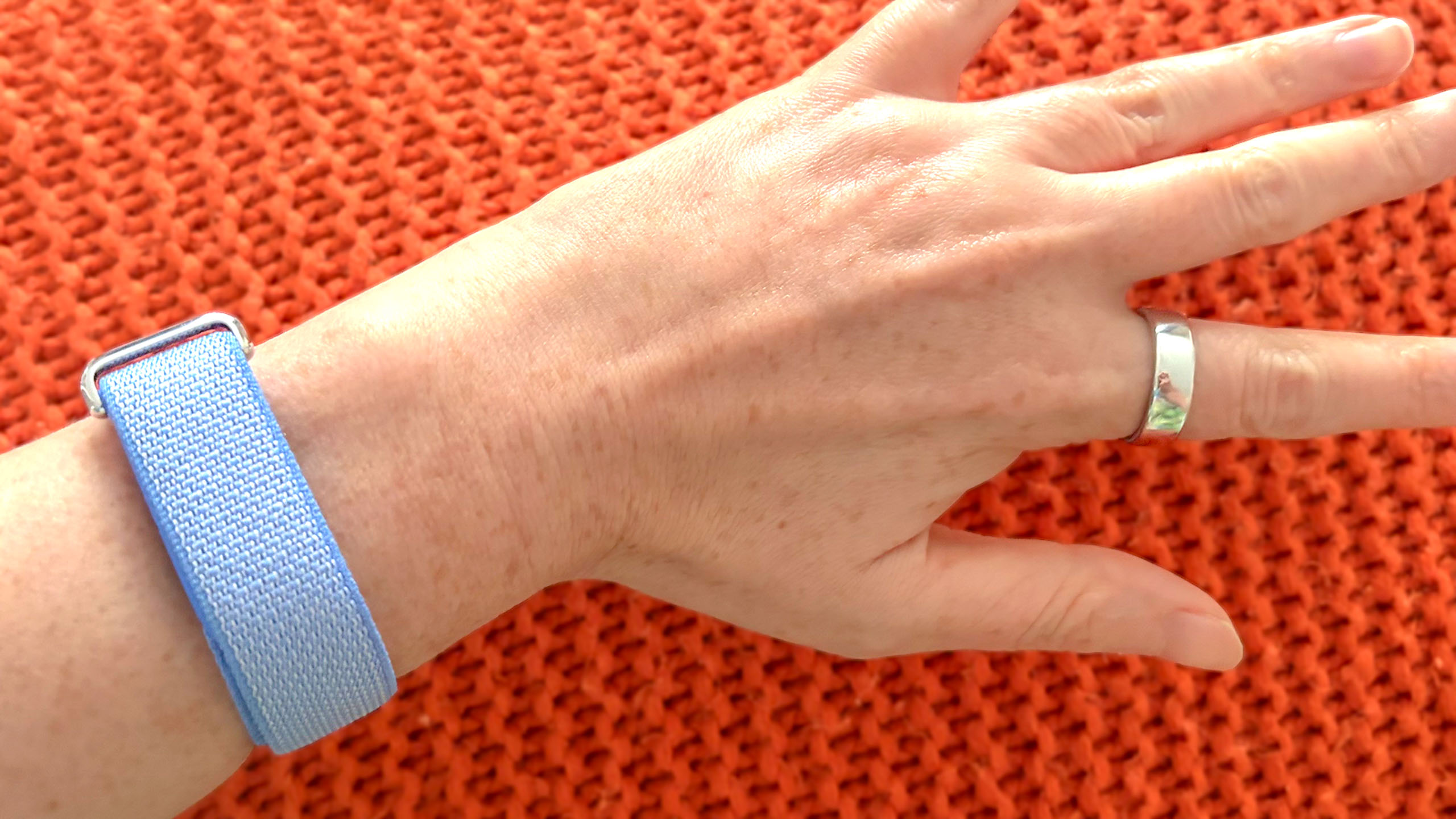 A close up of a hand wearing the Oura Ring 5 and a Fitbit Air