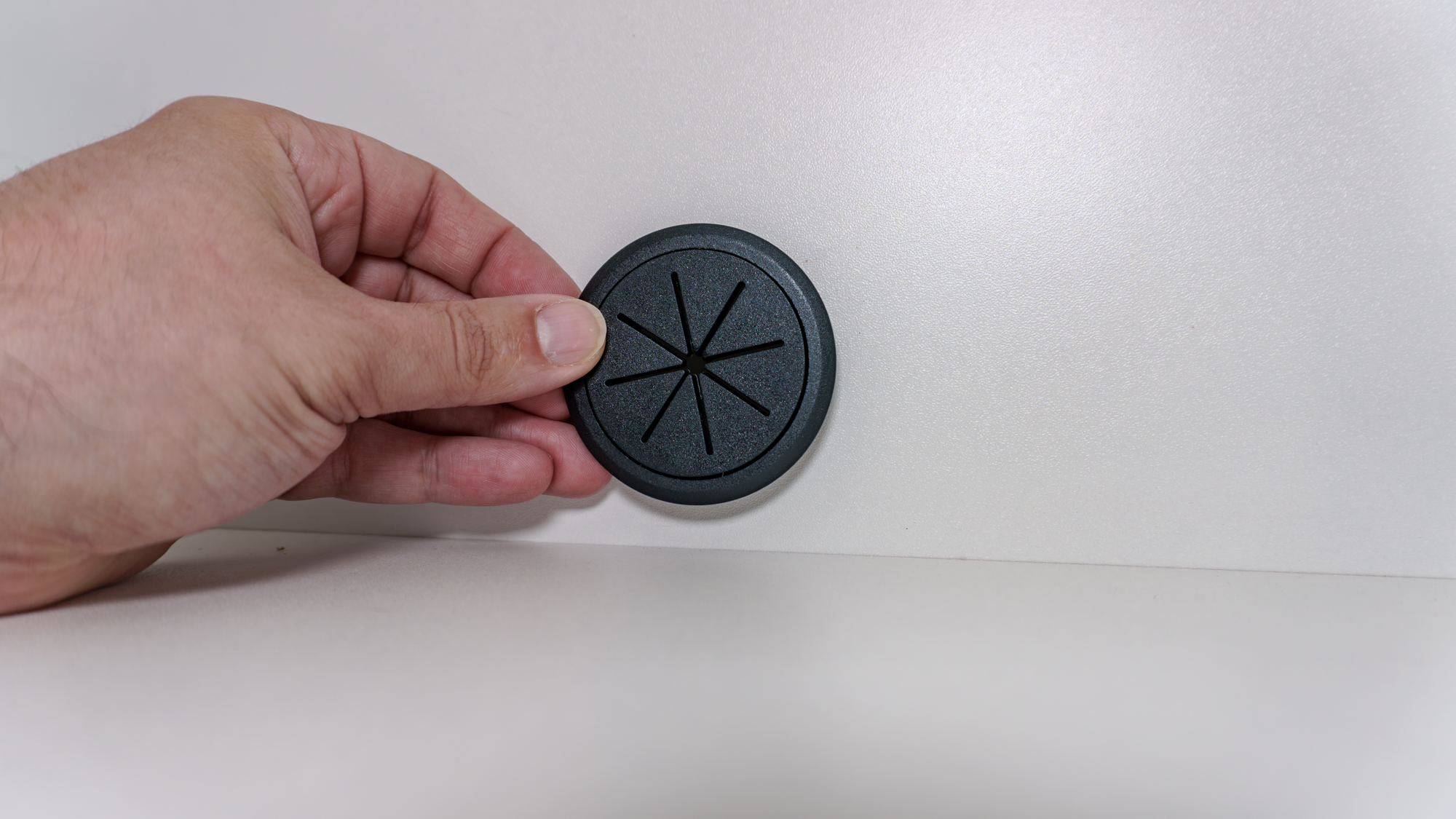 A person putting a 2-inch grommet into a hole they drilled at the back of a kitchen pantry cabinet