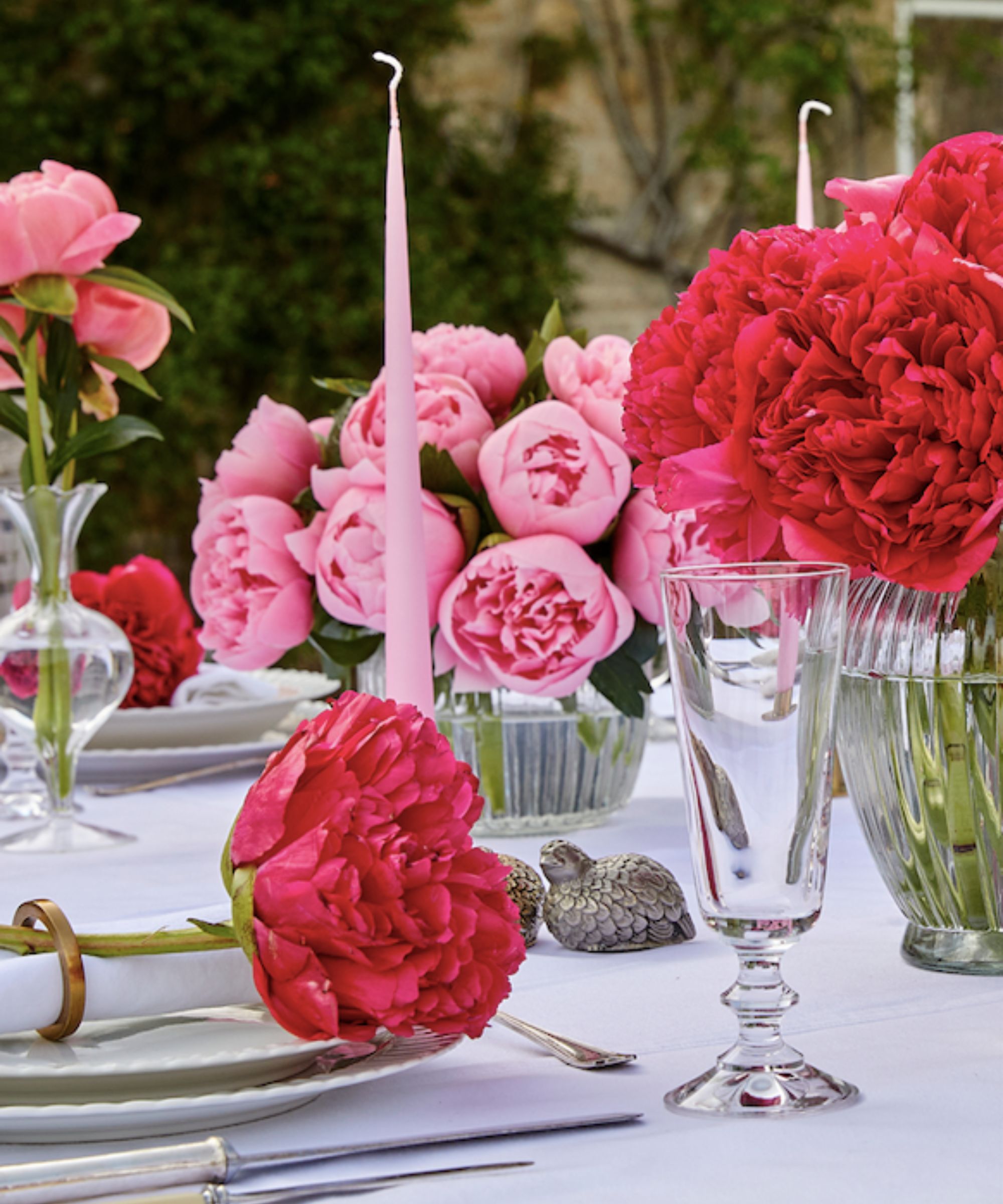 Bright red and pink peonies displayed as place settings and in glass vases on a formal table setting