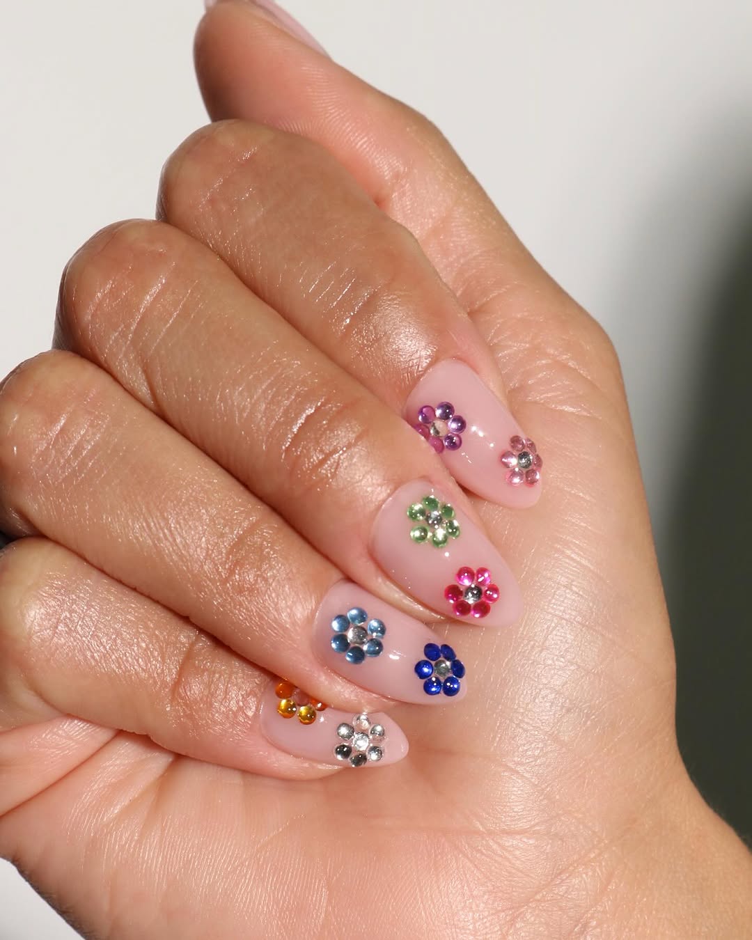 sheer nude nails featuring floral rhinestones of varying colors