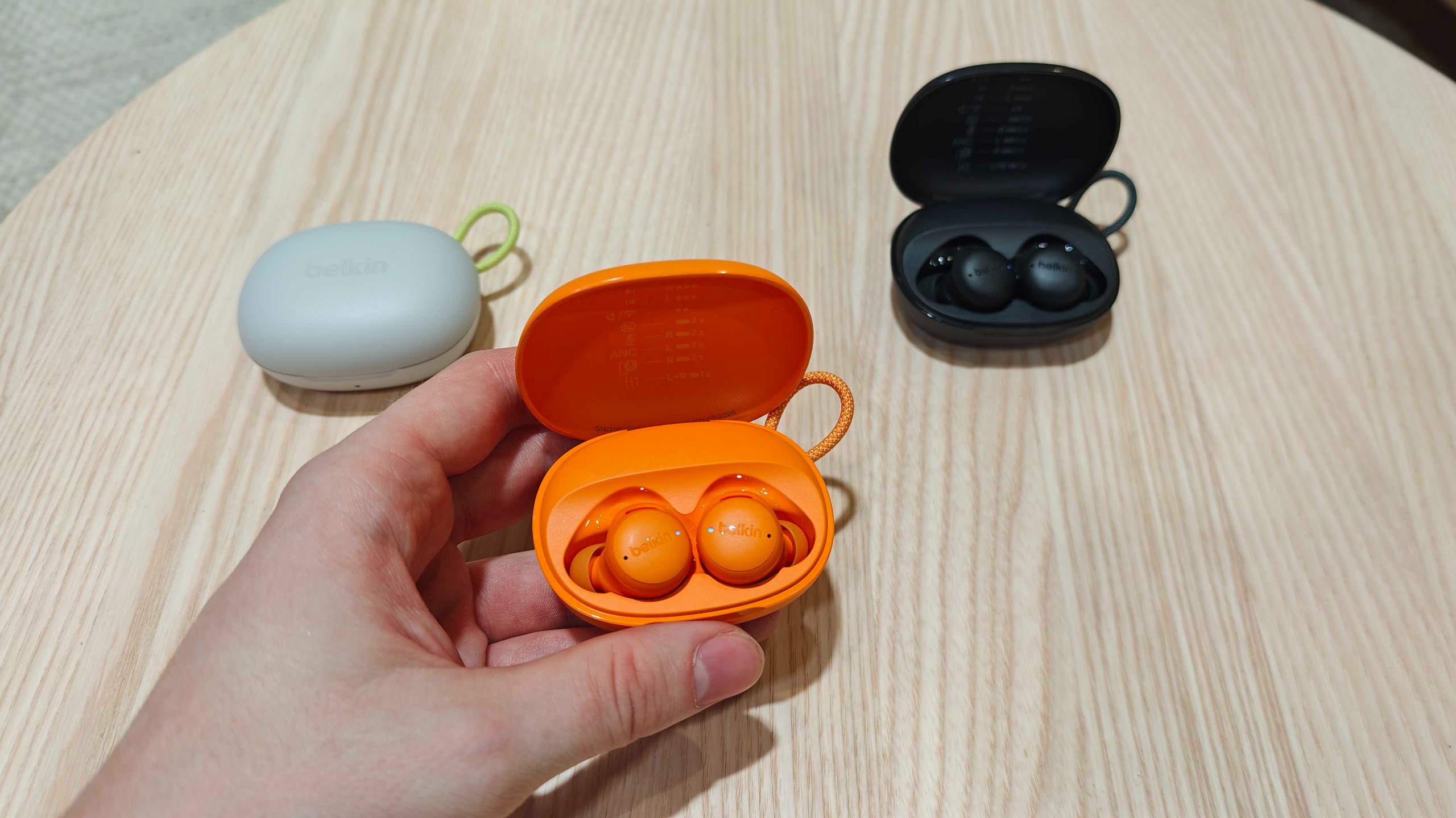 Belkin earbuds in orange held in a hand, with white and black options behind it, at IFA