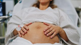 close up on the exposed belly of a pregnant woman propped up on a hospital bed and wearing a gown