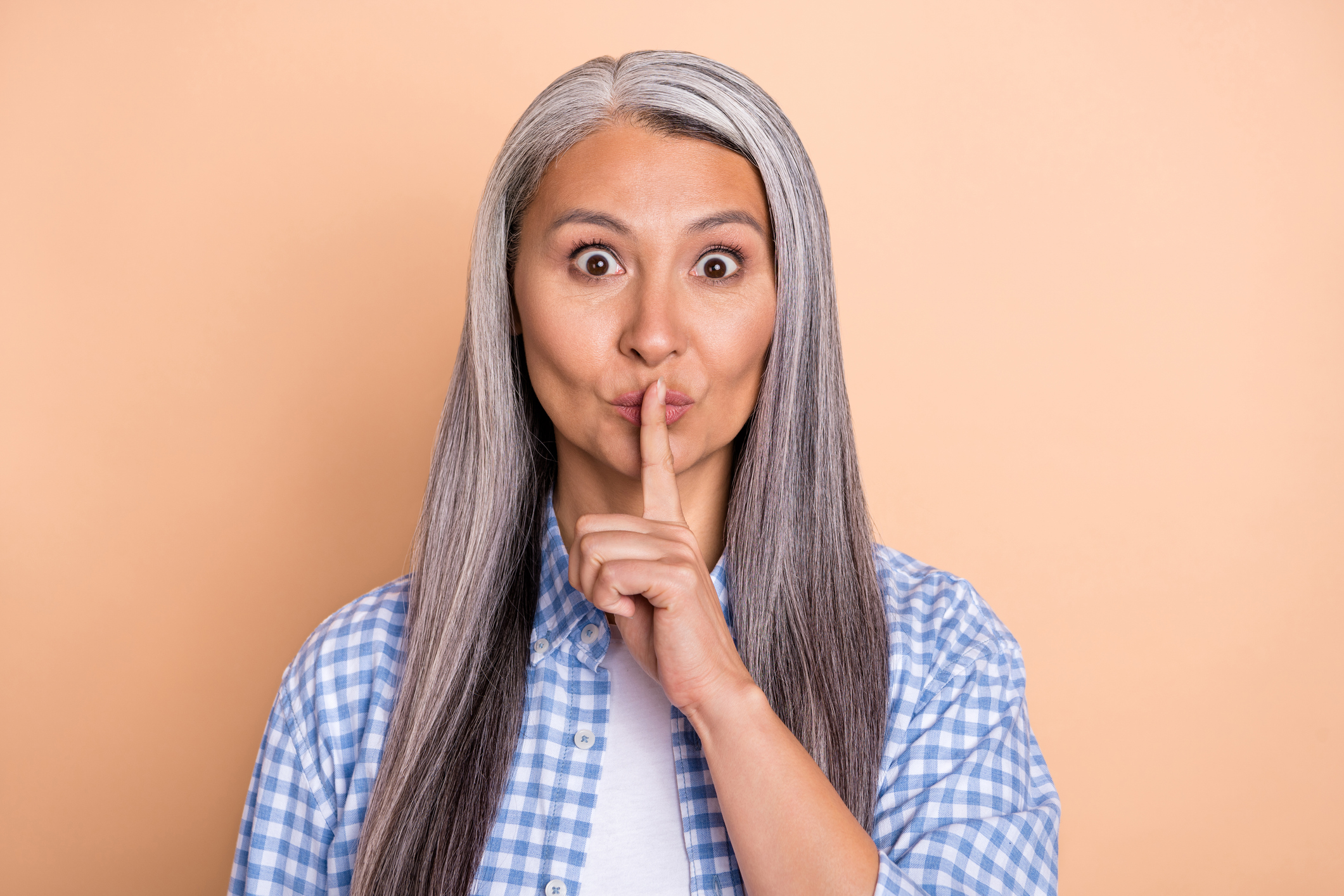 Photo of serious confident lady pensioner dressed checkered shirt finger lips asking keep silence isolated beige color background.
