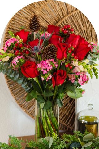 A bouquet of red and pink flowers with greenery in a clear vase.