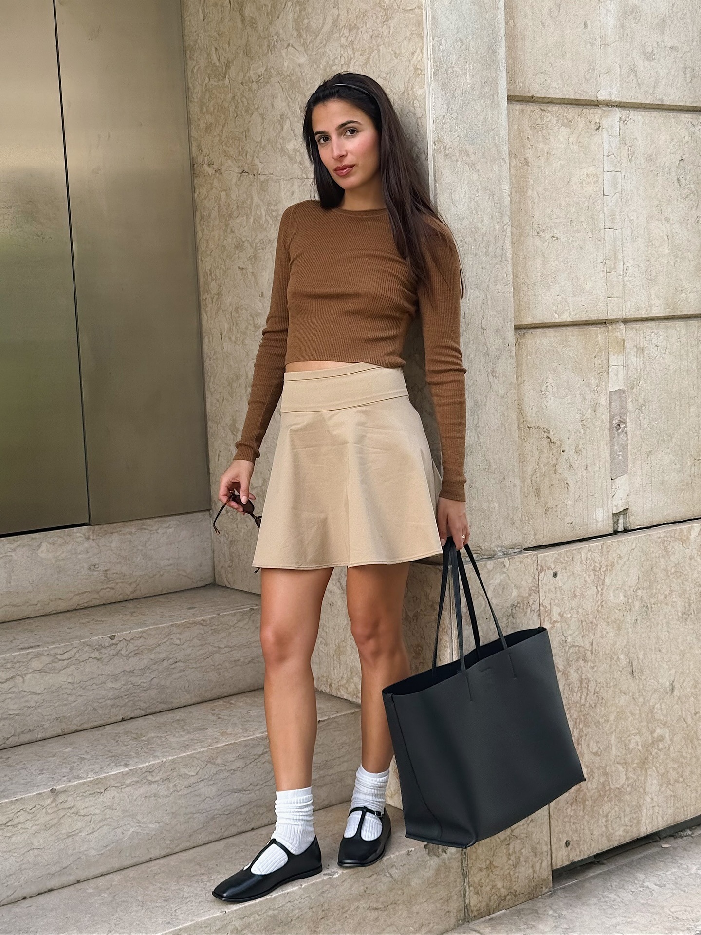Influencer @tamaramory wears a longsleeve top with a beige miniskirt and black t-bar ballet flats.