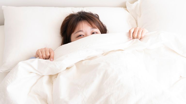 How to clean a duvet: woman in bed poking her head out from under the duvet