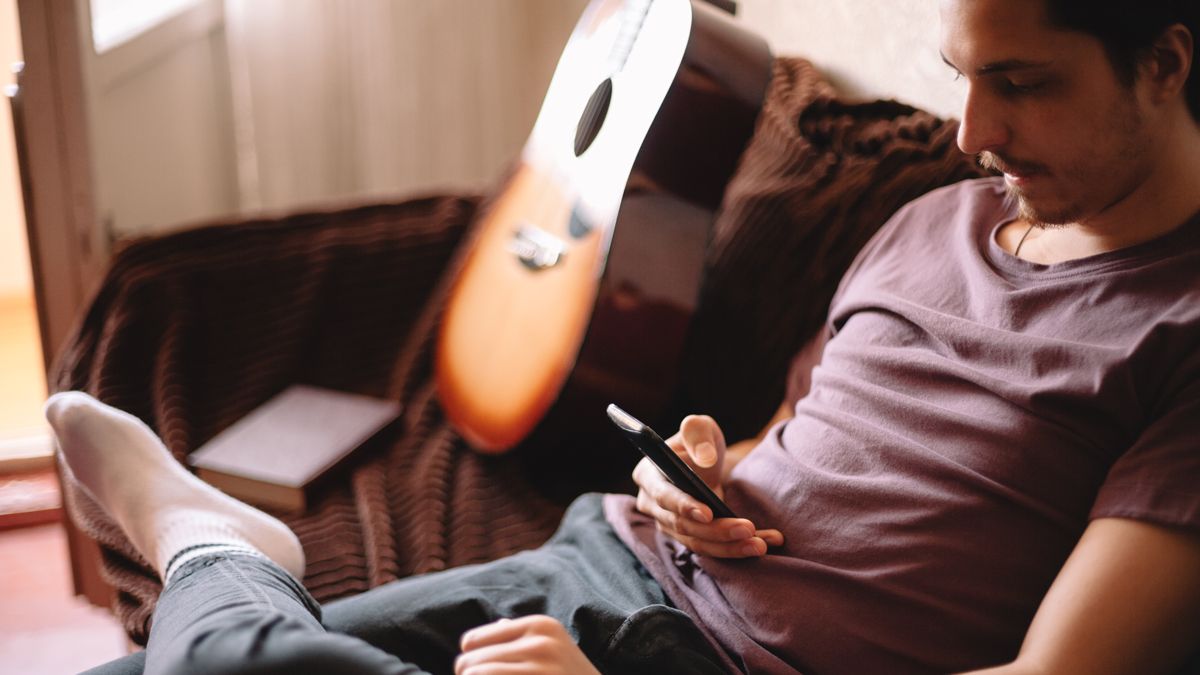 Young man using smart phone while sitting at home with guitar in background