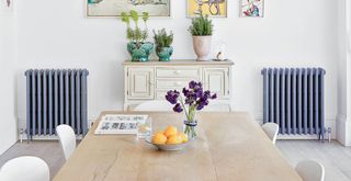 White dining room with blue cast iron radiators and a wooden dining table