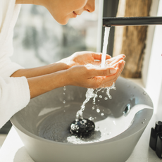 Best cleanser woman in white bath robe washing her face over a round sink 