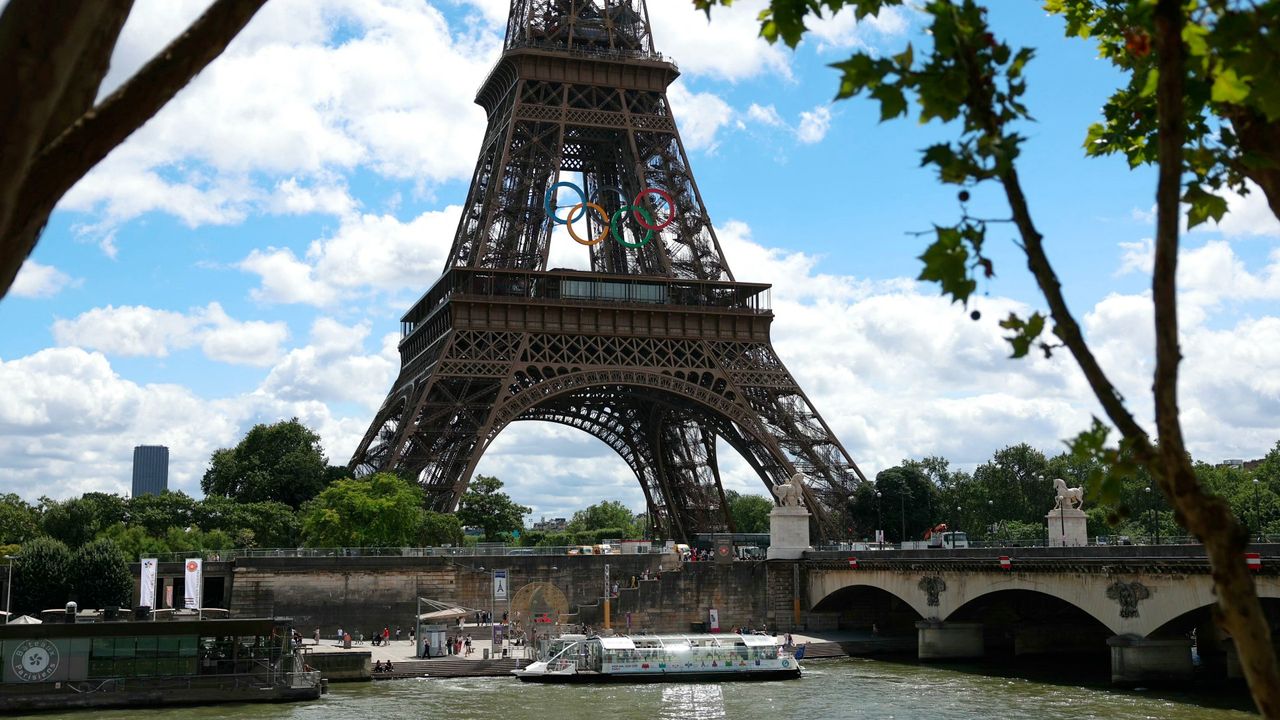  Seine river bus boat docks in front the Eiffel Tower adorned with Olympic rings 