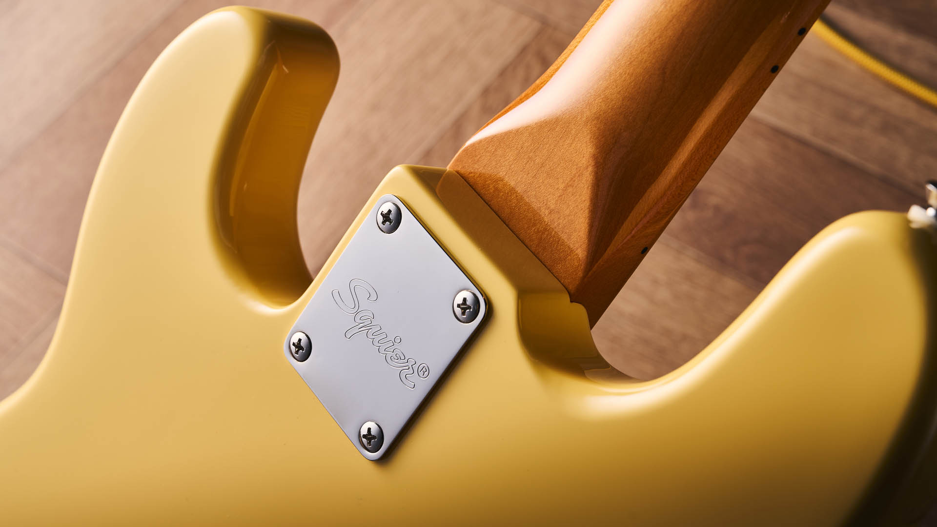 The Squier Classic Vibe Telecaster Bass is a fine-looking four-string in a custard-colored Vintage White, and is here photographed in close-up, against a plain wooden background. It has a single Wide Range humbucker.
