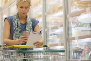 Woman with shopping trolley looking at phone and list