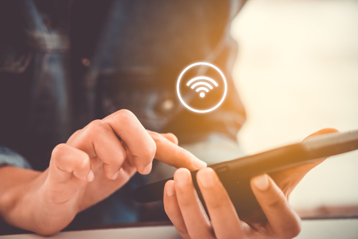 A person touching a spartphone screen with a Wi-Fi signal logo floating above it