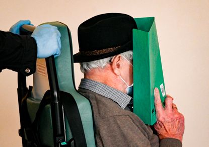 Bruno Dey, a former SS-watchman at the Stutthof concentration camp, covers his face as he is brought in a wheelchair to a courtroom for a hearing in his trial on March 20, 2020 in Hamburg, no