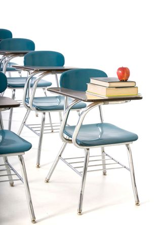 Empty classroom desk/chairs, one with books and apple. 