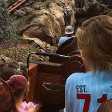 The back of Gigi Hadid wearing a blue jersey and her daughter Khai wearing pink Minnie ears riding a rollercoaster at Disney World