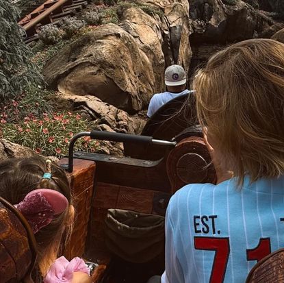 The back of Gigi Hadid wearing a blue jersey and her daughter Khai wearing pink Minnie ears riding a rollercoaster at Disney World