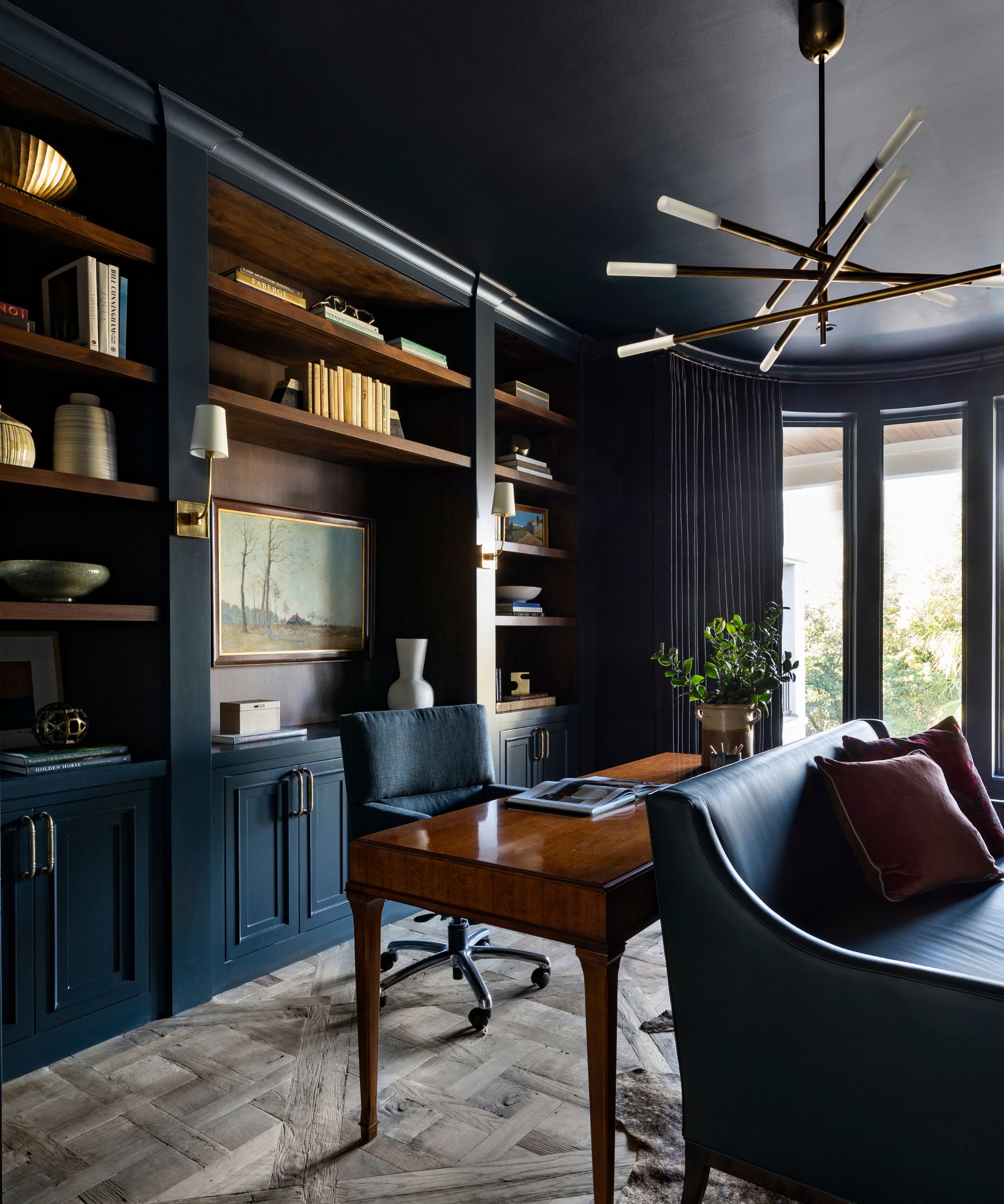 A dark and moody home office room with color-drenched walls, wood floors, and built-in shelving.