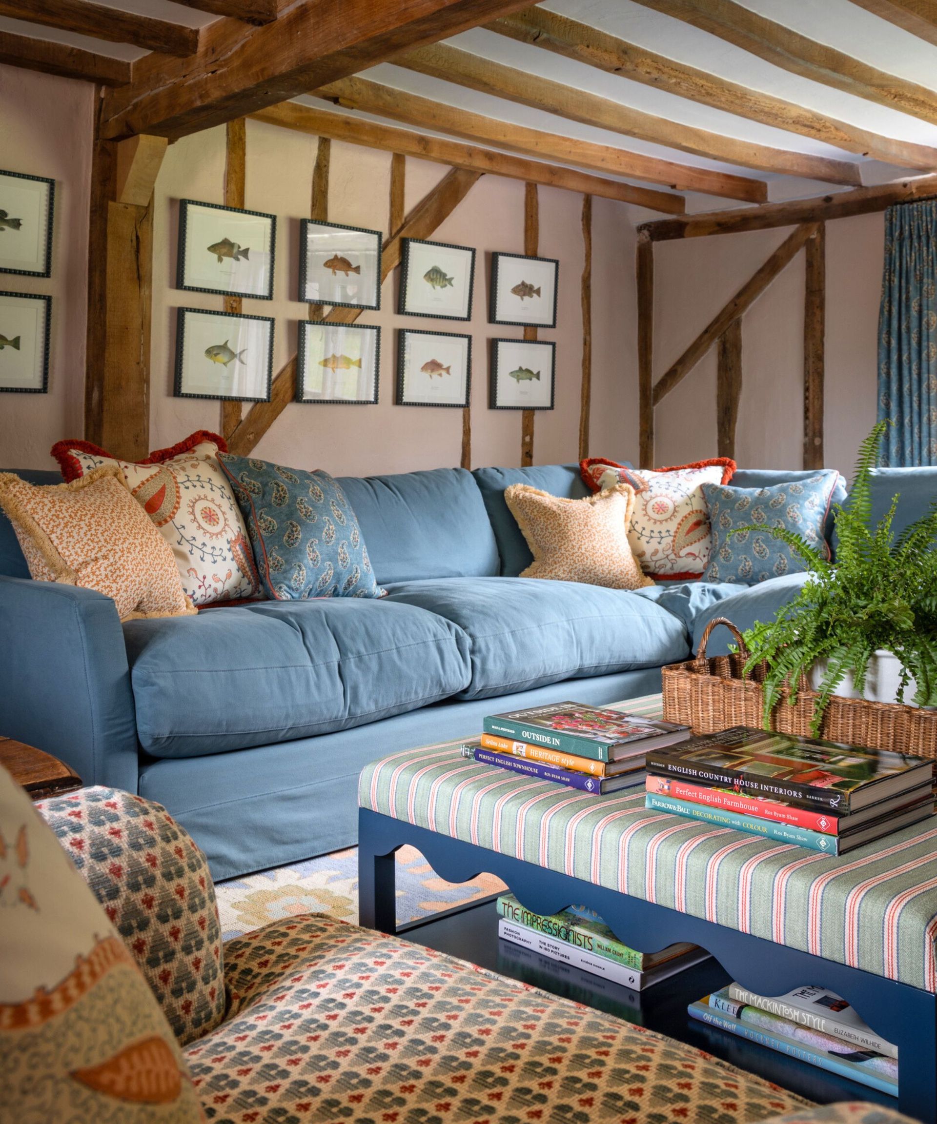 A cottage living room with soft pink walls and old beams, furnished with a deep blue linen sofa and a large ottoman