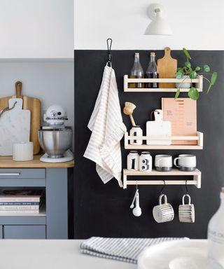 Black wall of kitchen with wooden shelving attached holding kitchen accessories