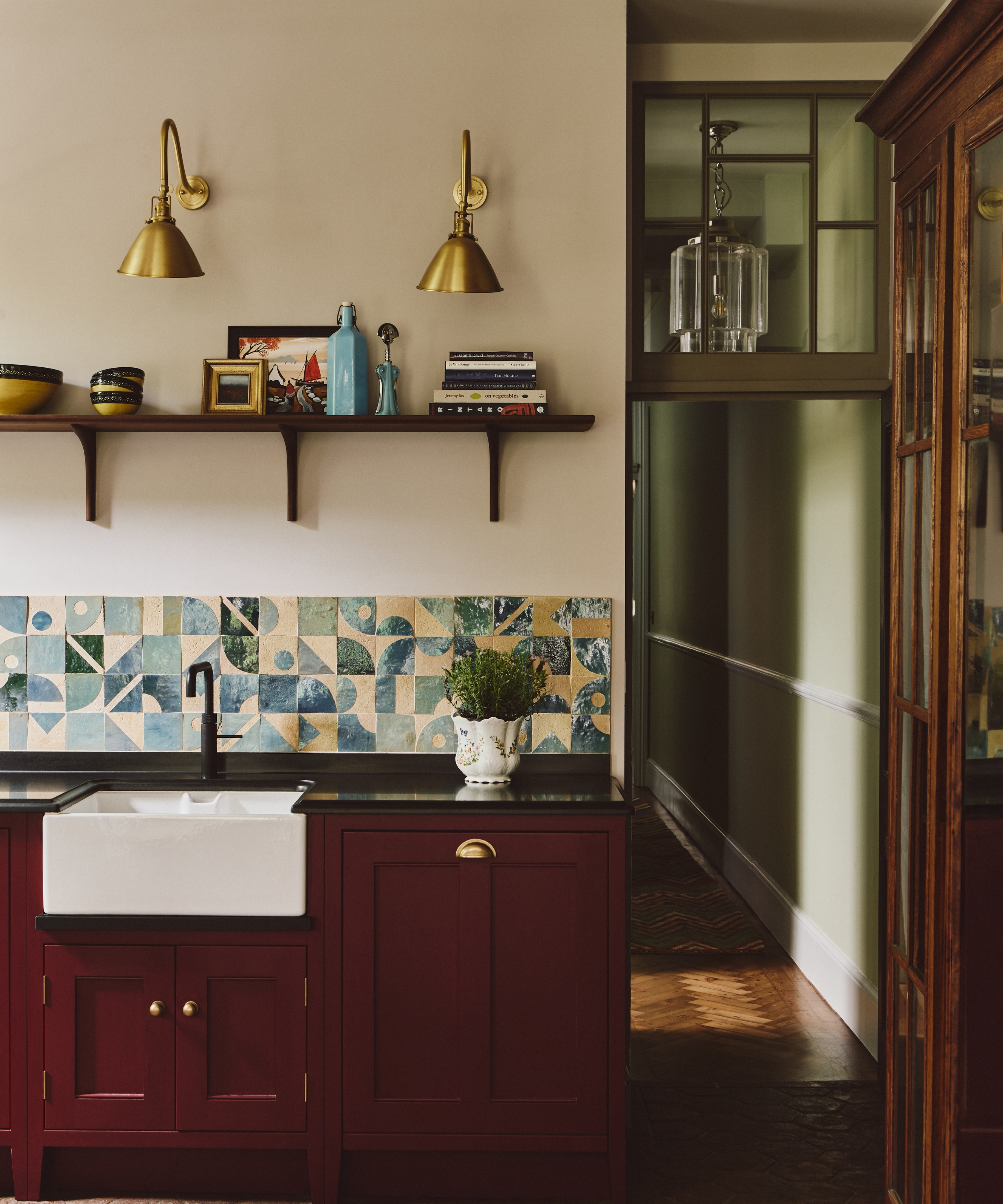 A small kitchen with arm white walls, blue pattered backsplash tiles, and oxblood cabinets