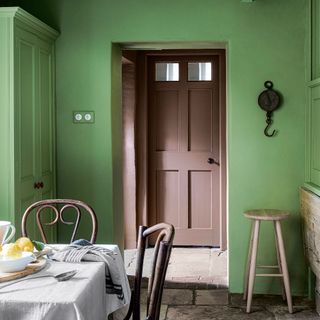 kitchen with green walls and cabinetry looking through doorway to brown door