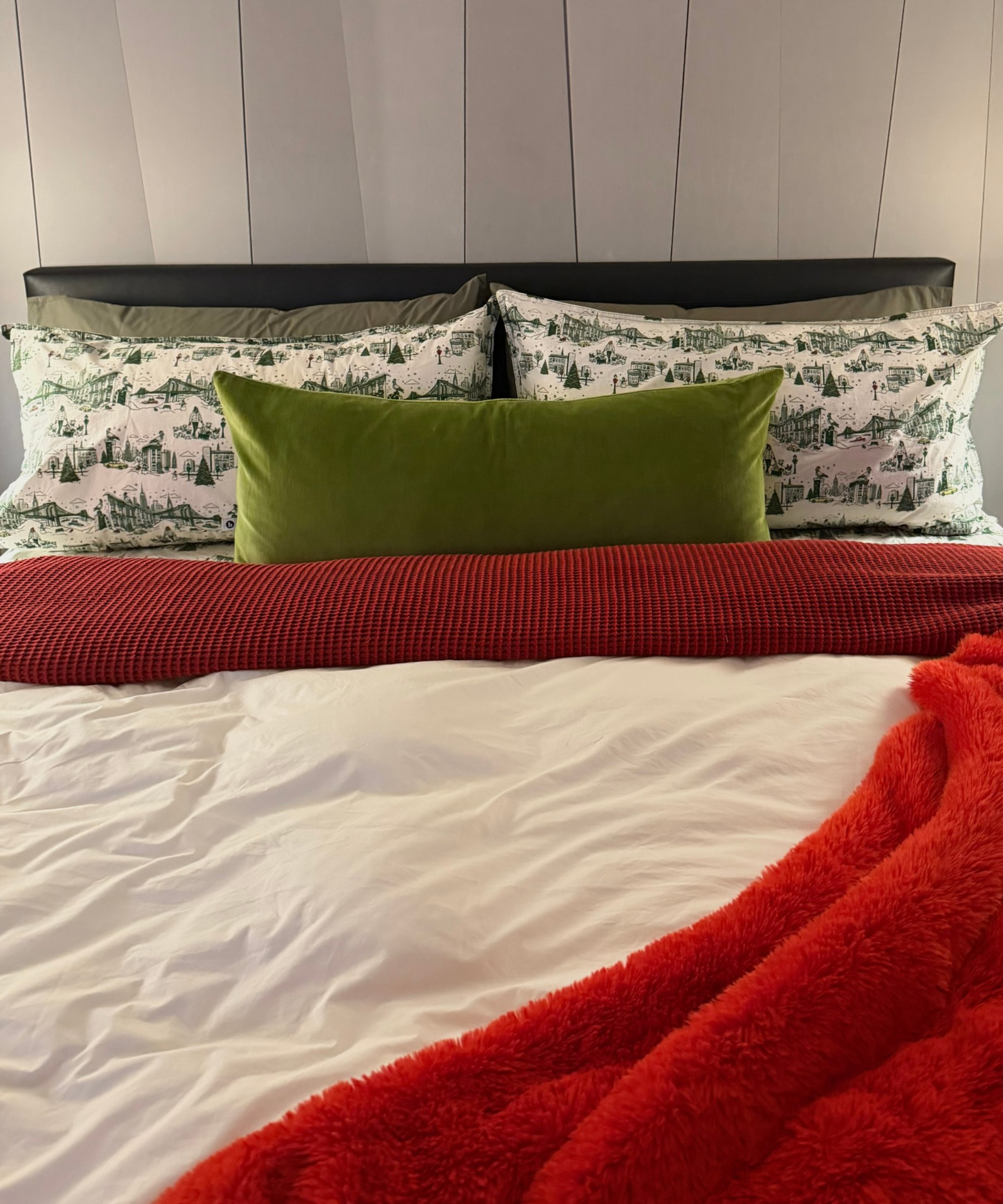 Christmas bedding featuring winter-motif green toile-printed sheets paired with a moss green lumbar pillow and bright red throw blankets.
