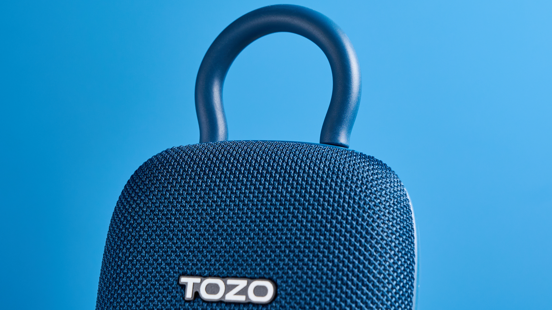 Tozo PE1 speaker in blue with built-in clip photographed on a blue background.