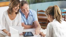 An older couple work with a financial adviser on paperwork at their kitchen table.