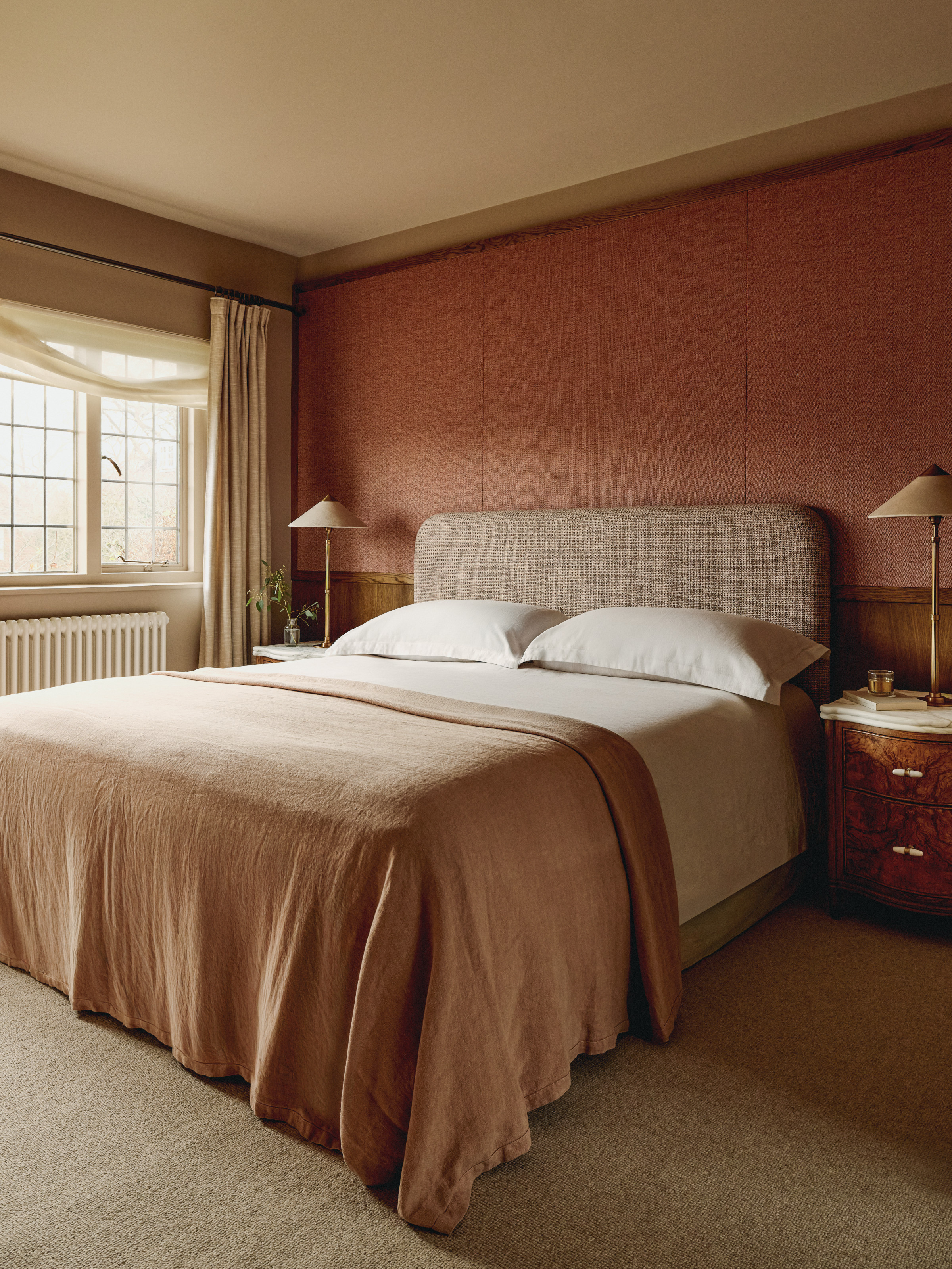 Bedroom with rust wallpaper, beige upholstered headboard and plaster pink throw