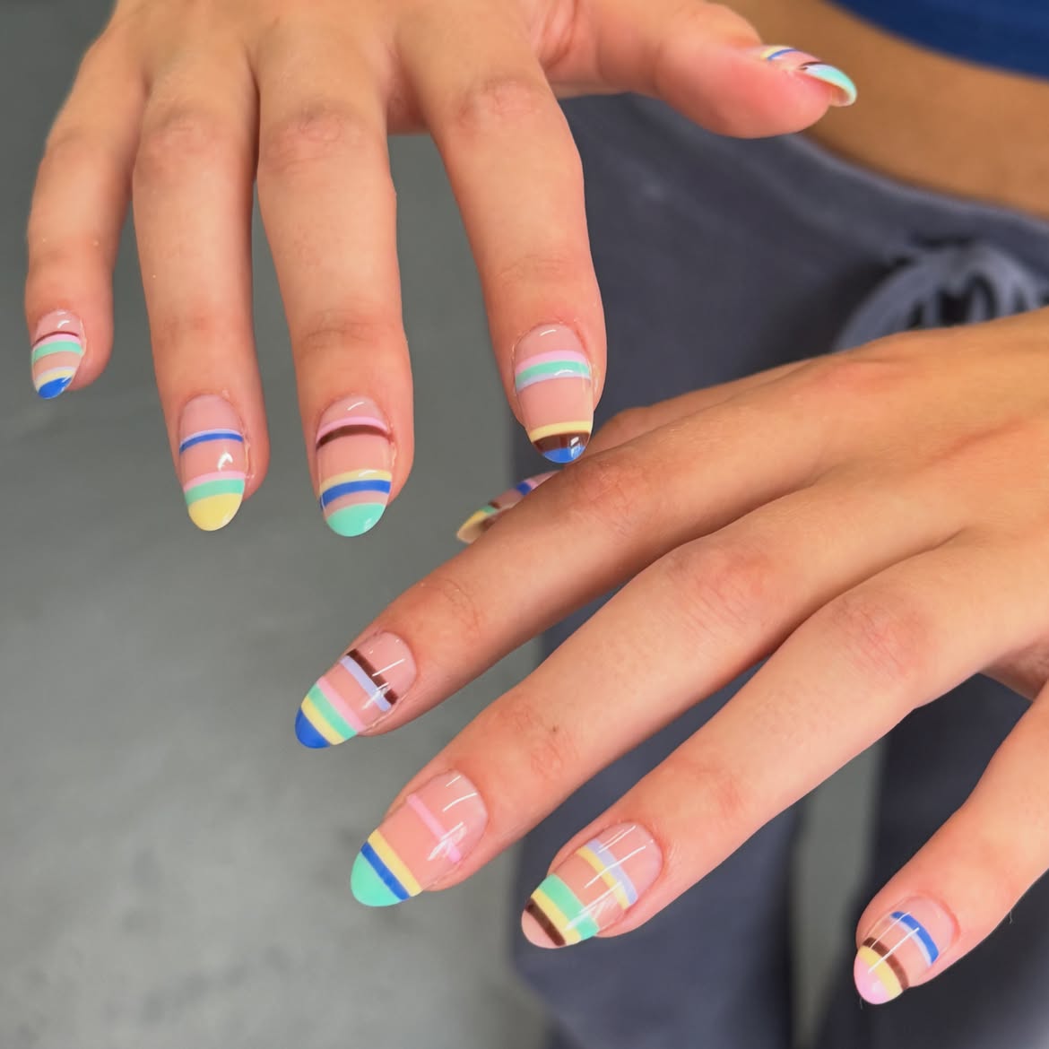 Sheer almond nails decorated with pastel stripes in pink, blue, yellow, brown, and green