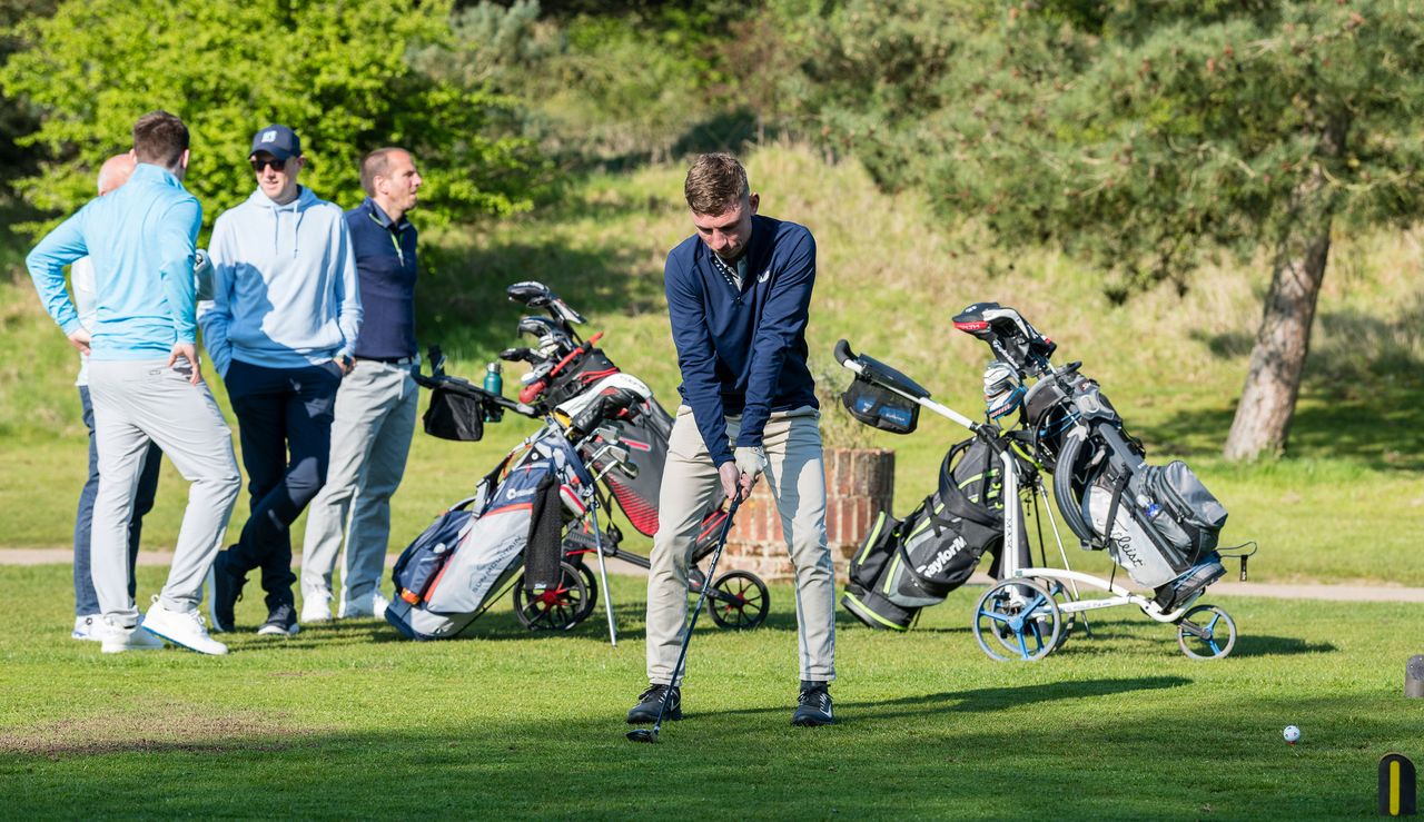 A golfer lines up on the tee box, whilst his buddies chat behind him